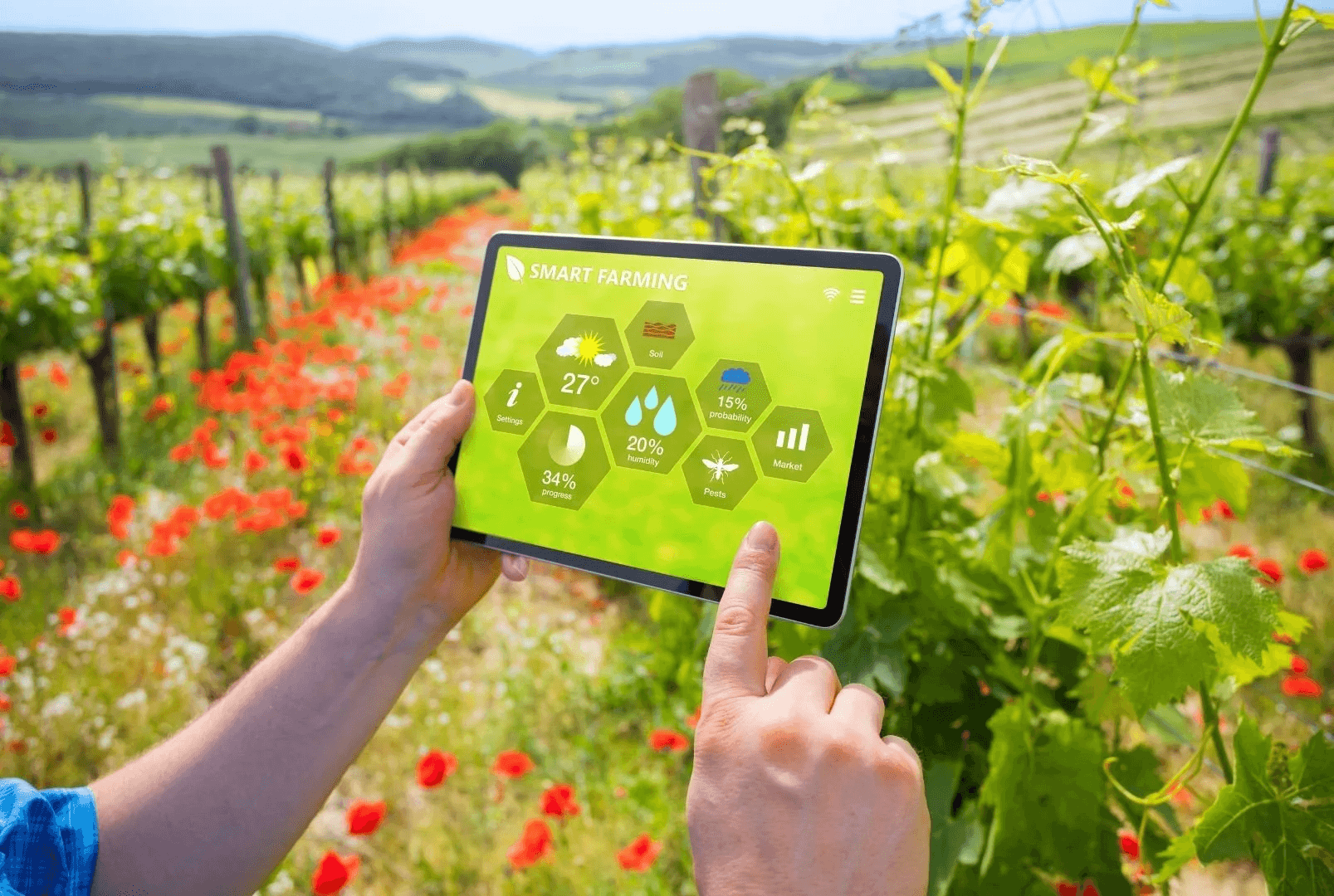 A tablet displaying a smart-farming dashboard with weather, soil and humidity tiles, held over a vineyard in bloom.